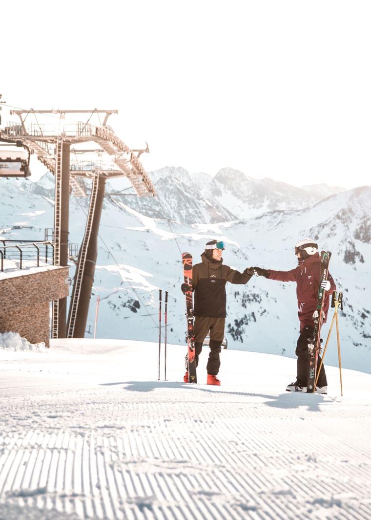 Two skiers fist bumping near ski lift station in the snow-covered Alps